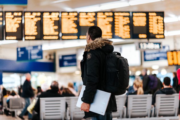 Man met winterjas kijkt naar bord met vertrektijden op vliegveld