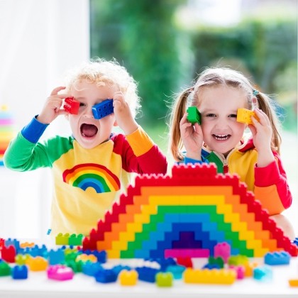 2 peuters hebben pret met regenboogkleur-blokken (Duplo) bouwen. 