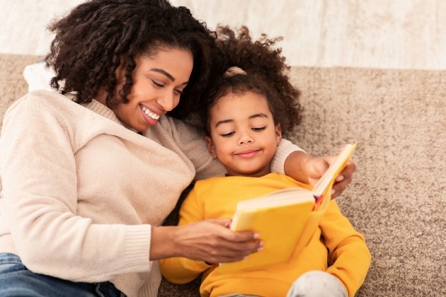 Moeder en kind zitten samen een boek te lezen op de bank.